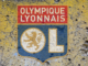 Logo de l'Olympique Lyonnais sur un mur criblé de trous et de lézardes.